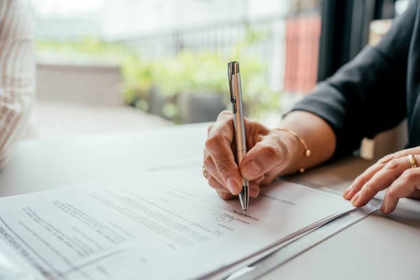 A woman signing a contract with a pen, representing Traveling Notary Services in a professional setting.