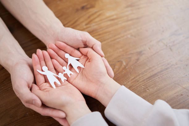 Hands grasp paper family cutouts, representing the concept of no medical exam life insurance for families.