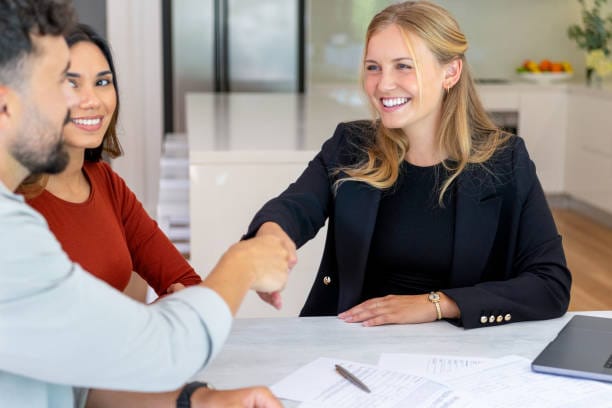 A woman shakes hands with a man and another woman at a table, discussing no medical exam life insurance options.