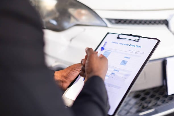 A man in a suit reviews car insurance documents while standing next to a vehicle.